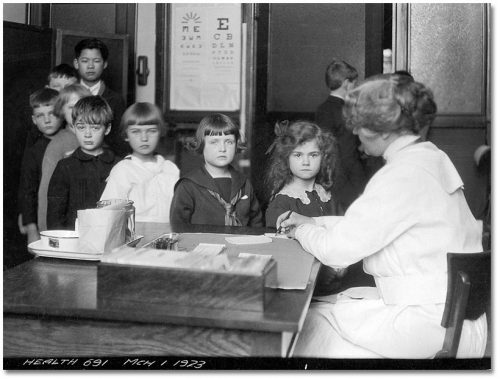 Children line up in front of a nurse at a desk.