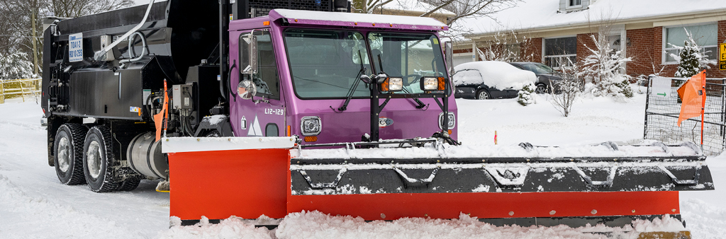 A large colourful snow plow clearing snow from a residential road