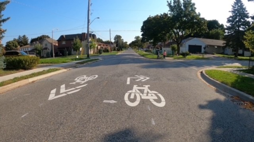An example of on-street shared lane markings in a similar neighbourhood. The pavement markings consist of white paint showing a bicycle and directional arrows in the middle of the road. showing a