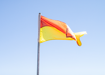 A flag on a flag pole. The flag has two strips - red on top and yellow below.