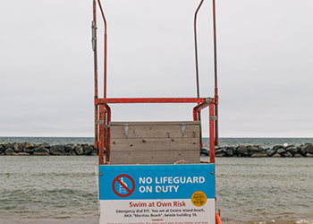 A lifeguard stand with a No Lifeguard on Duty sign. There is no flag attached to the stand.