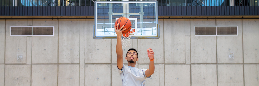 Person dunks a basketball in an indoor gym.