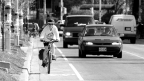 A lady biking in a bike lane with cars in the lane next to her.