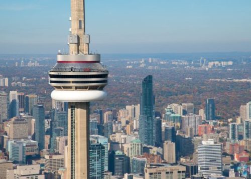 CN Tower in foreground against a backdrop of city buildings and trees on a hazy day.