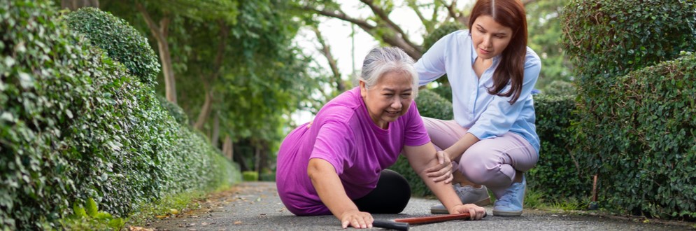 Asian senior woman fell down and lying on ground. Caregiver present to support.