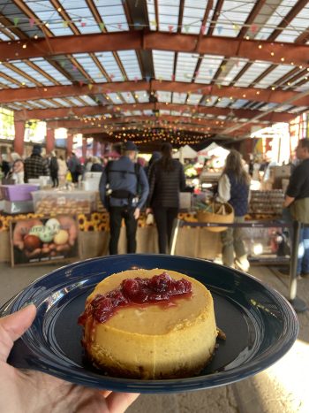 A dessert covered in syrup on a reusable plate with a crowd in a farmer's market ahead.