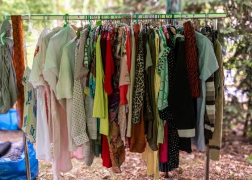 Bright and pastel clothes hanging on a clothing rack under trees
