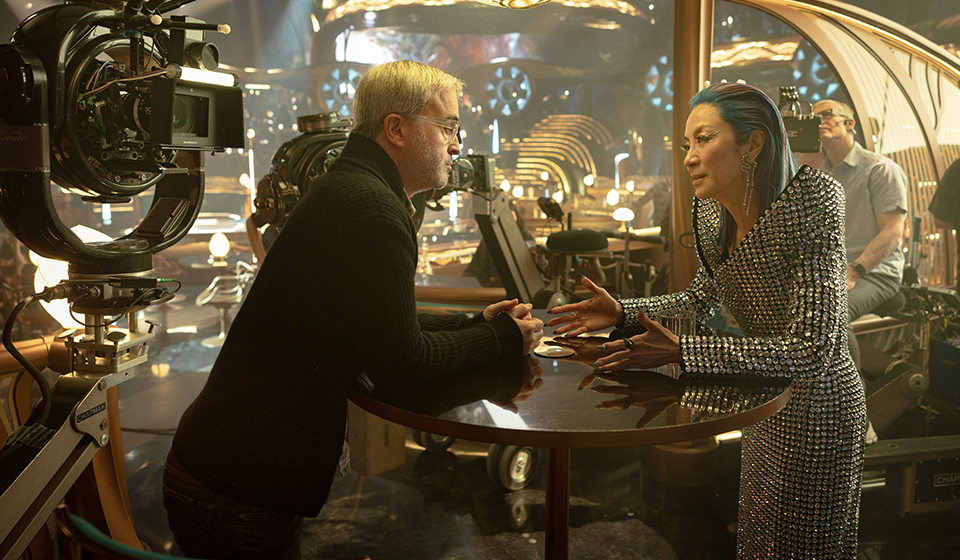 Two people dressed standing across from each other talking at a cocktail table.