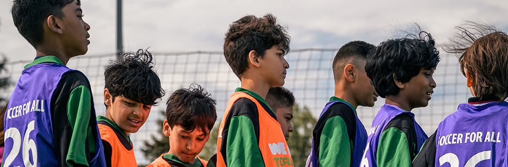 A group of kids outside wearing jerseys that read "Soccer For All"