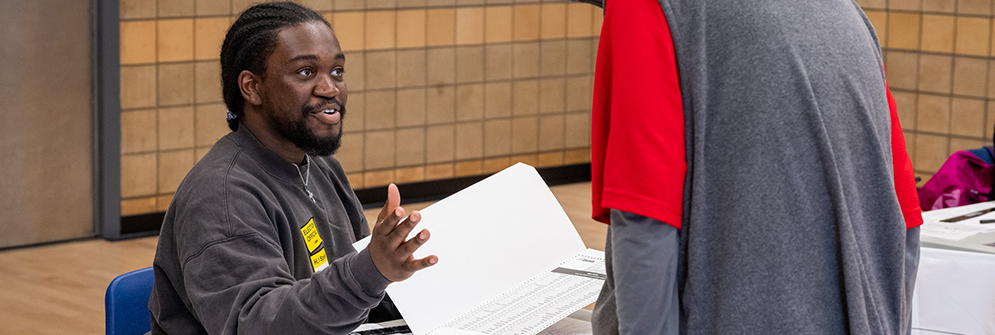 Smiling ballot officer, who is working in the voting place explaining information to an eligible voter.